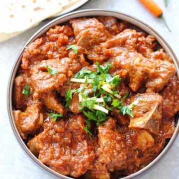 lamb karahi gosht in a bowl with roti on the side and two green chillies