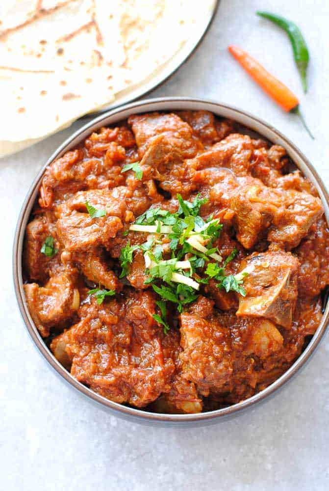 lamb karahi gosht in a bowl with roti on the side and two green chillies