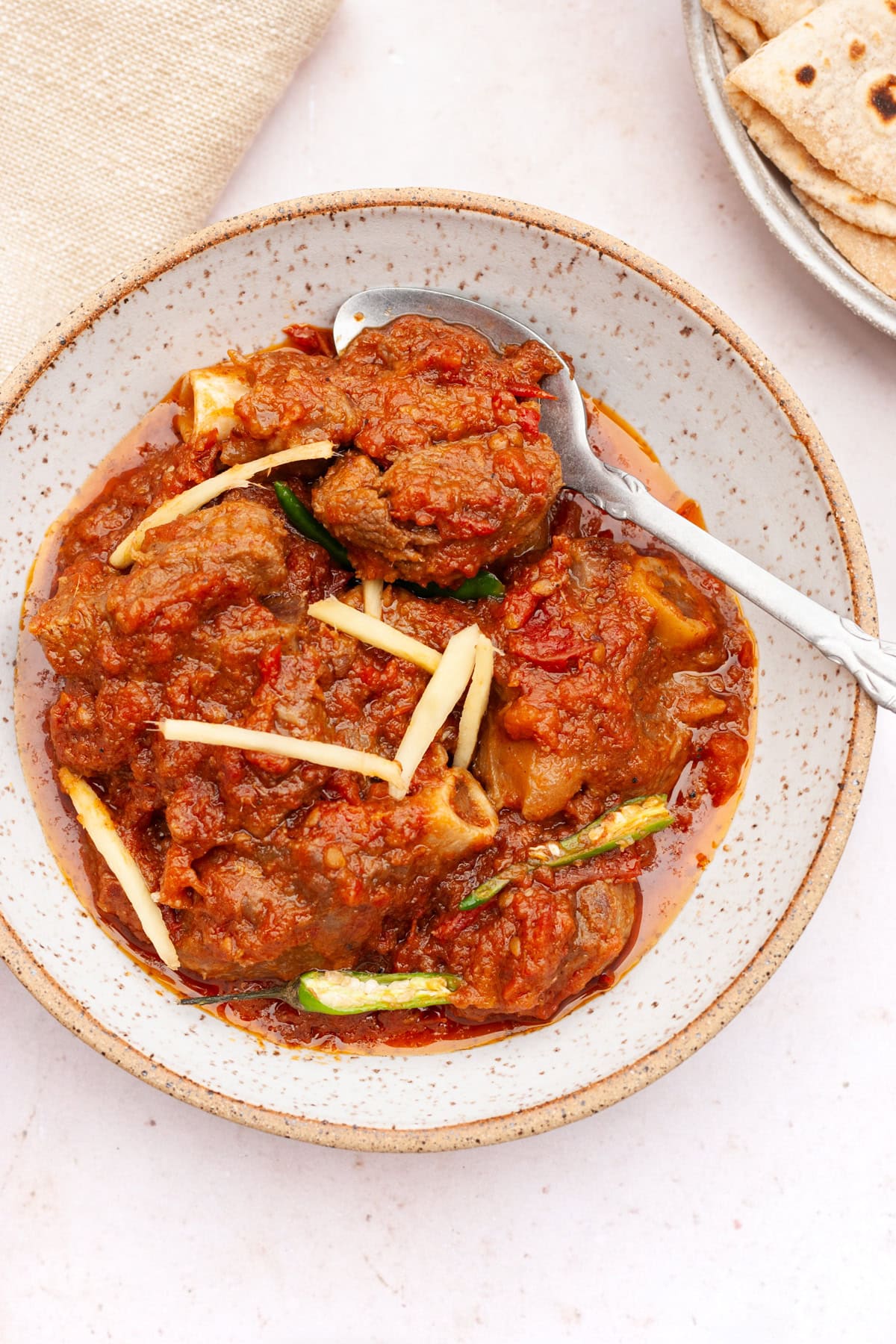 lamb karahi gosht in a bowl with roti on the side and two green chillies