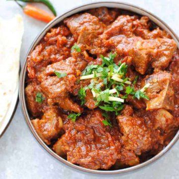 lamb karahi gosht in a bowl with naan and green chillies on the side