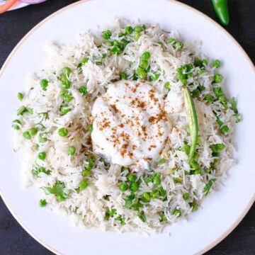Matar pulao in a plate with a dollop of raita on top.