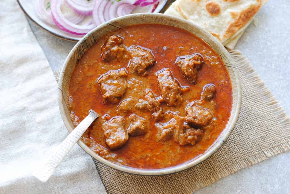 mutton korma in a bowl with onions and Indian bread