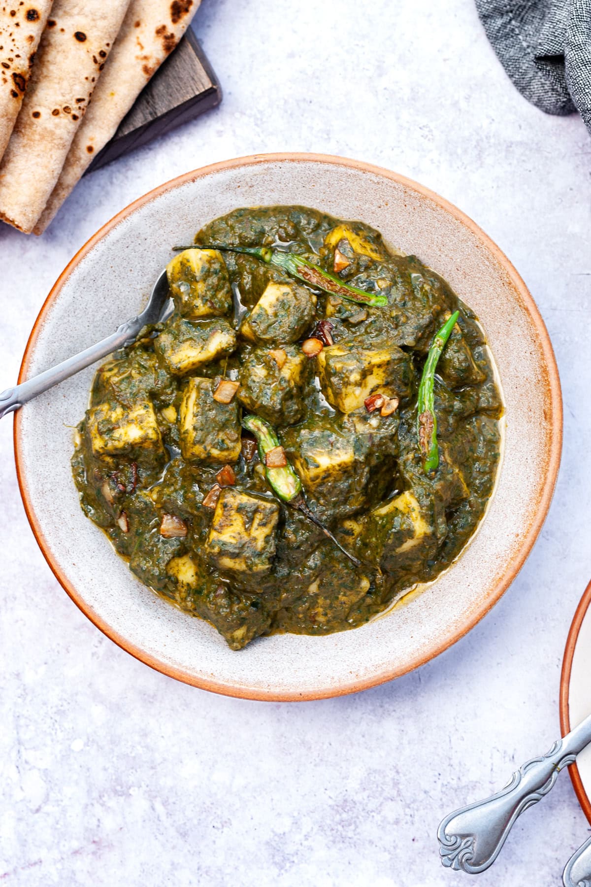 palak paneer in a bowl with salad and naan on the side