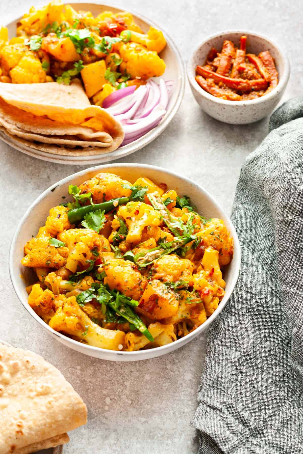 Aloo Gobi in bowl with roti and Indian pickles (achar) in small bowl.