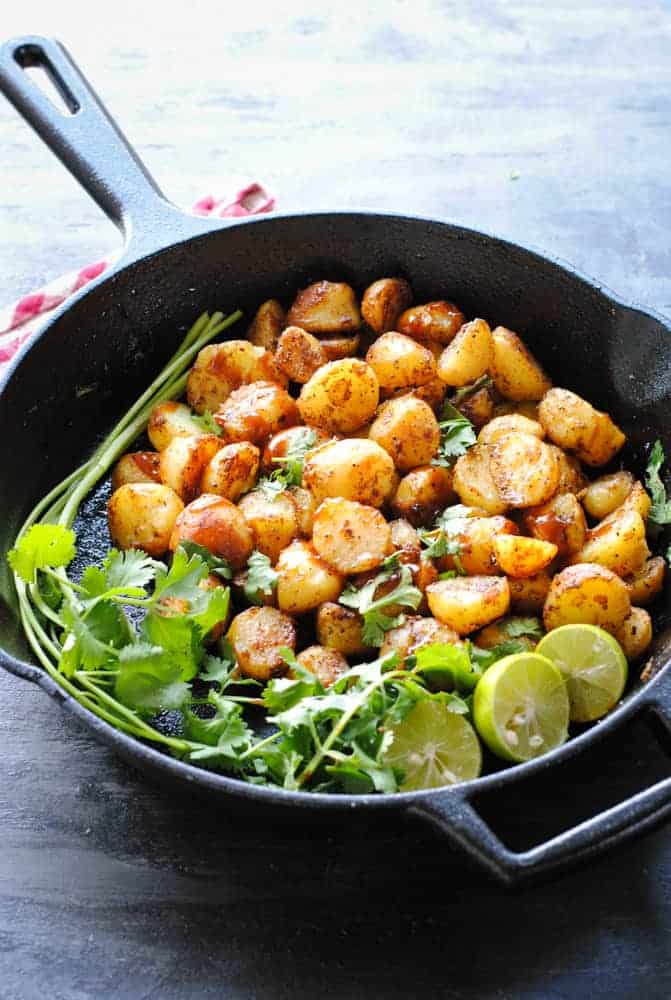 Aloo Chaat (Spicy Potatoes) in a skillet with lemon wedges and cilantro