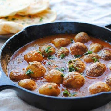 dum aloo (baby potatoes in gravy) in a skillet with naan on the side