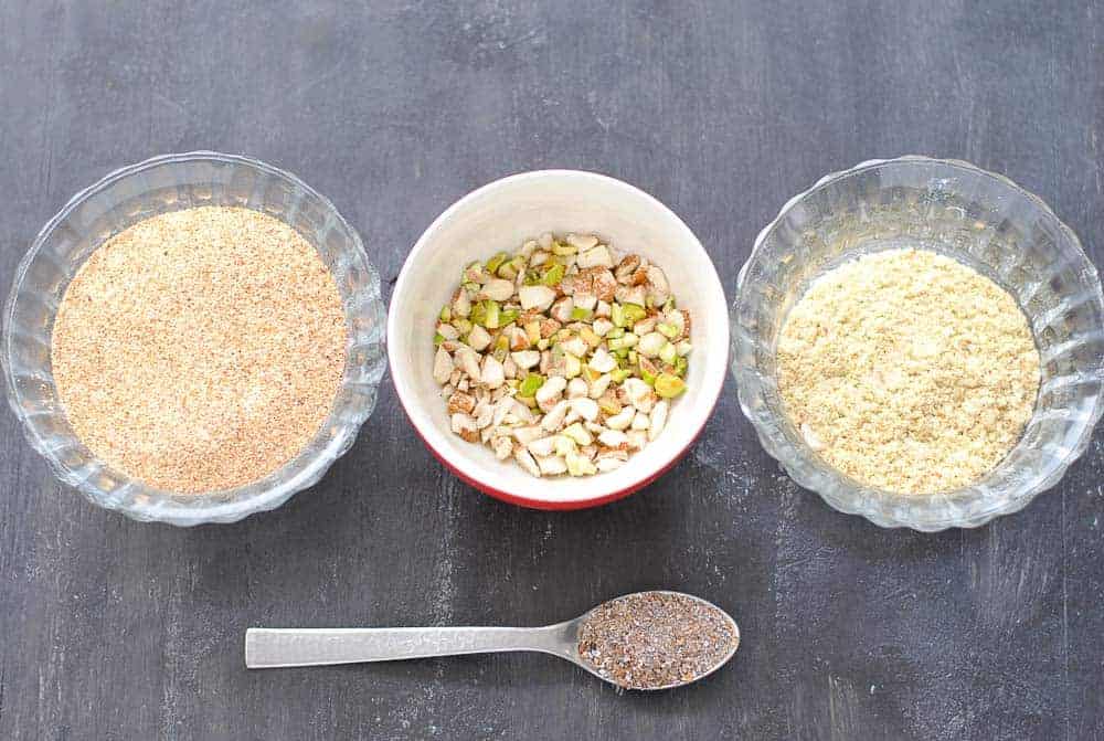 semolina, chopped nuts, ground nuts in three bowls and a teaspoon of cardamom powder. 