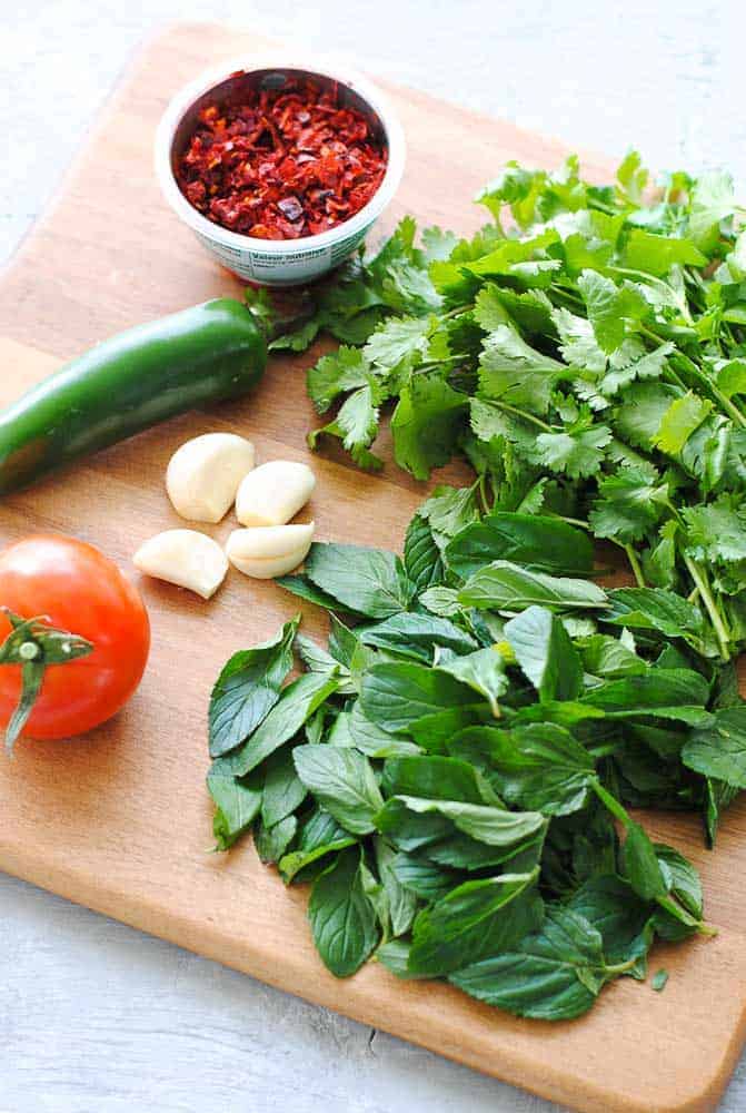 mint, cilantro, tomato, green chilli, crushesd red chilli and garlic on a wooden chopping board