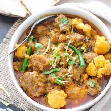 Gobi gosht in a bowl with naan on the side
