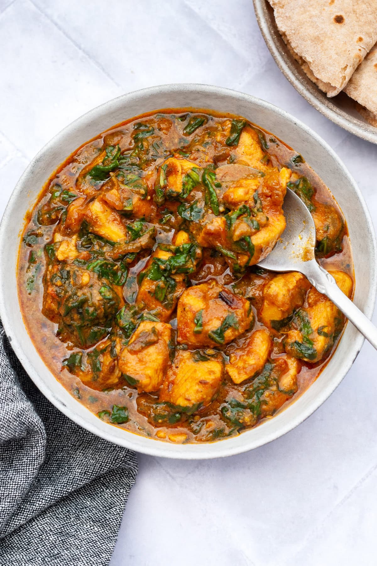 palak chicken in a bowl with a spoon and naan and rice on the side