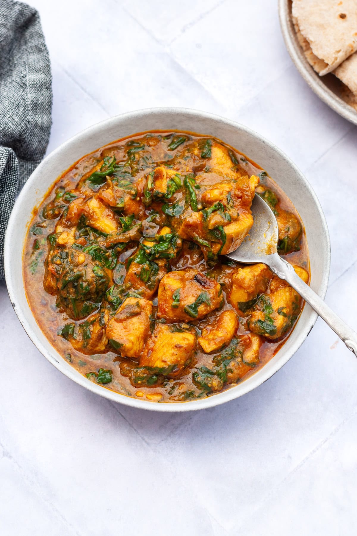 palak chicken in a bowl with naan and rice on the side