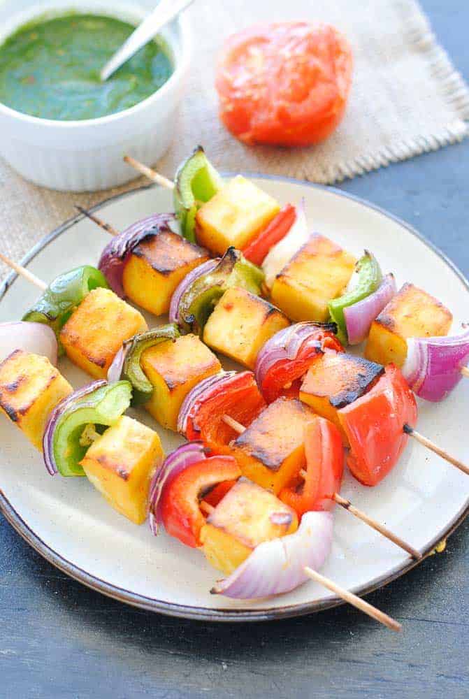 paneer, capsicum and onion skewers on a plate with green chutney and a tomato on the side