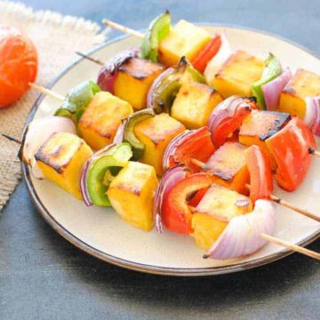 paneer kabab with capsicum and onion on a plate with green chutney and a tomato on the side