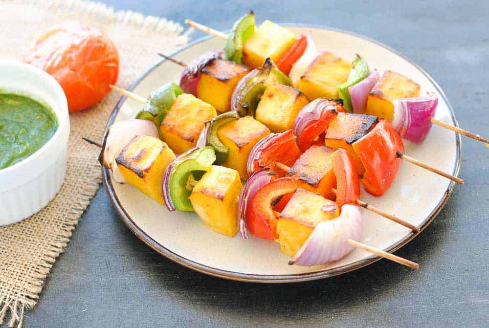 paneer kabab with capsicum and onion on a plate with green chutney and a tomato on the side