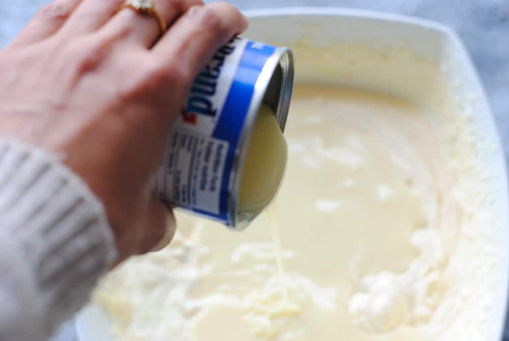 whipped cream in a bowl with a hand pouring condensed milk from the top