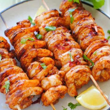 tandoori shrimp skewers on a plate with lemon wedges and lettuce