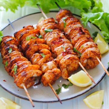 tandoori shrimp skewers on a plate with lemon wedges and lettuce