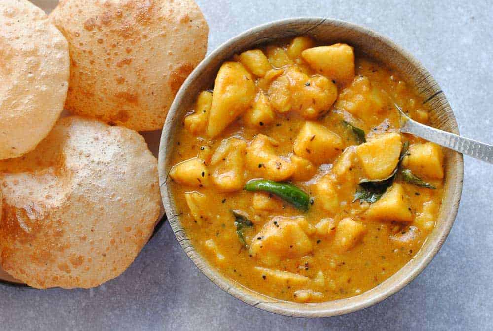 potato curry in a bowl with pooris on plate beside it