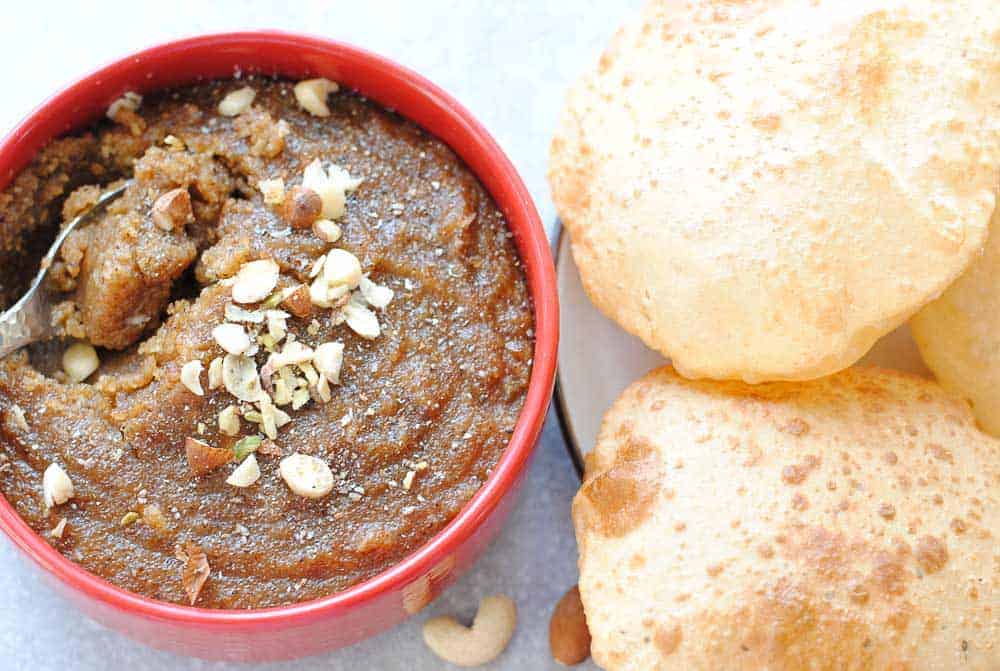 semolina halwa in a red bowl with pooris on the side