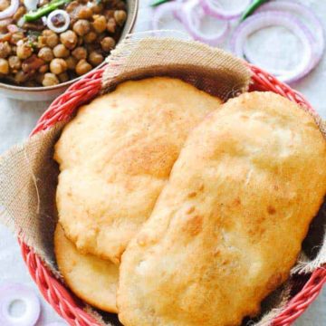 bhature in a red basket with a bowl of chole and onions on the side