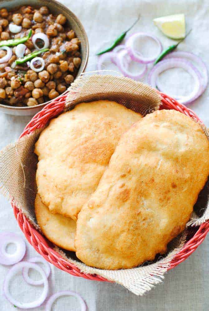 bhature in a basket with a bowl of curried chickpeas in the background