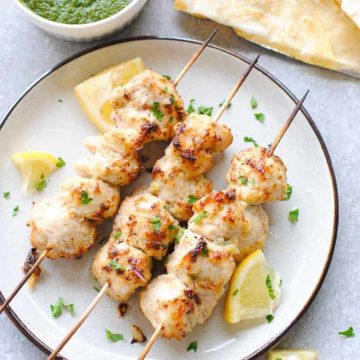 chicken malai tikka skewers on a plate with green chutney and roti on the side