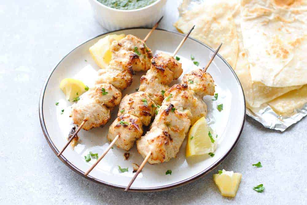 murgh malai skewers on a plate with green chutney and roti in the background