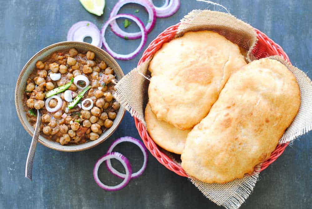 chole (chickpea curry) in a bowl with bhature in a red basket beside it