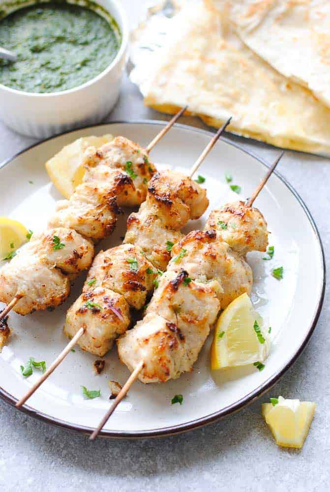 chicken malai tikka skewers on a plate with green chutney and naan on the side