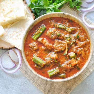 okra with meat curry in a bowl with roti onions and cilantro on the side