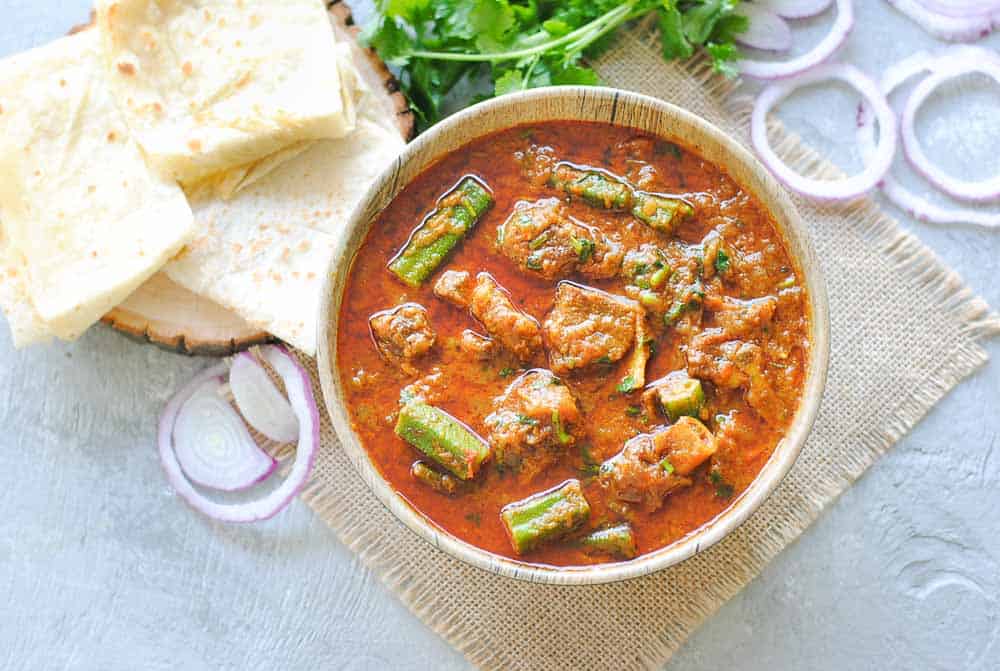 okra with meat curry in a bowl with roti onions and cilantro on the side