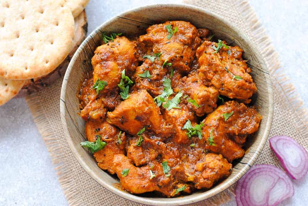 chicken achari in a bowl with naan on the side