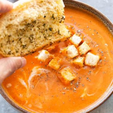 tomato soup with croutons, hand with bread piece over it