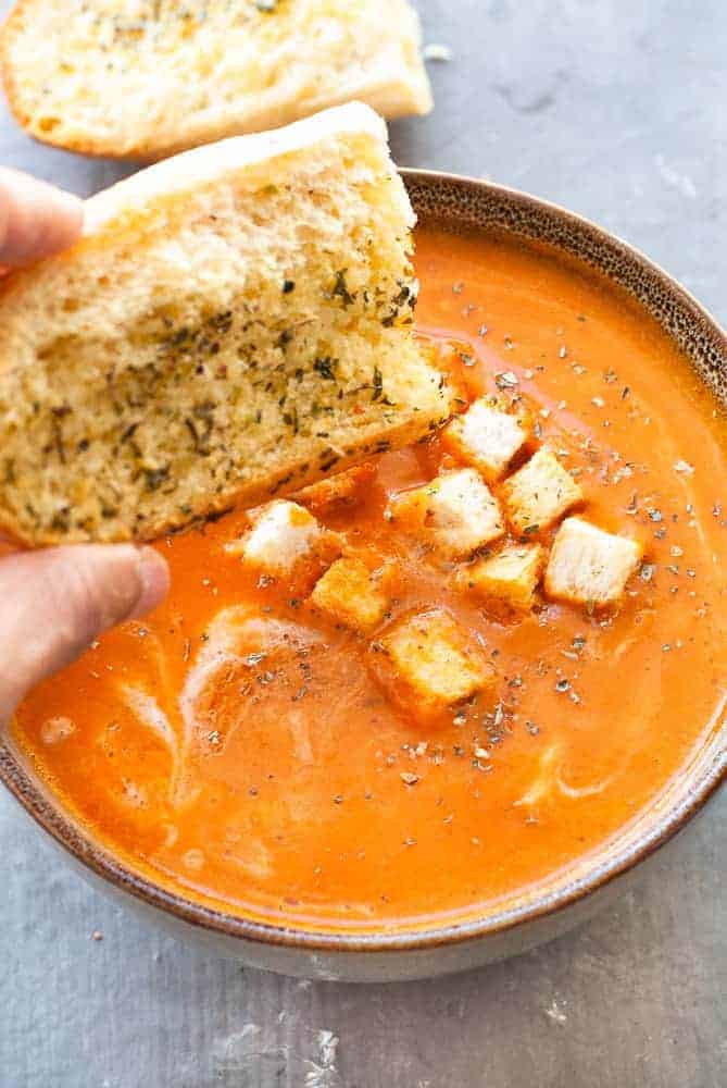 tomato soup with croutons, hand with bread piece over it