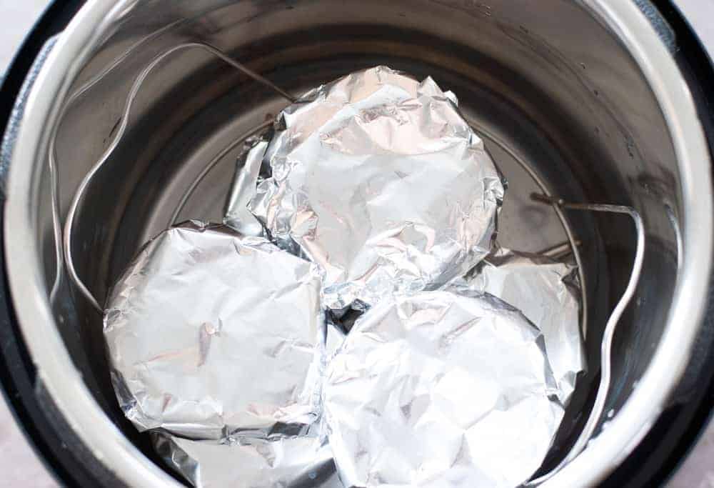 hamburger patties wrapped in aluminum foil on a trivet in instant pot