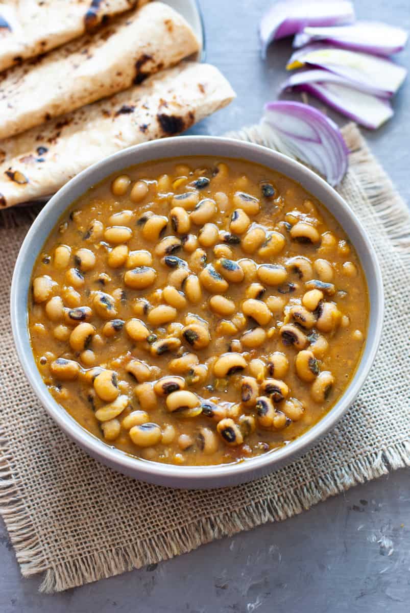 black eyed peas in a bowl with some Indian bread and sliced onions in the background.