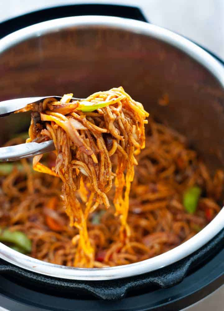 a pair of tongs with lo mein over an instant pot