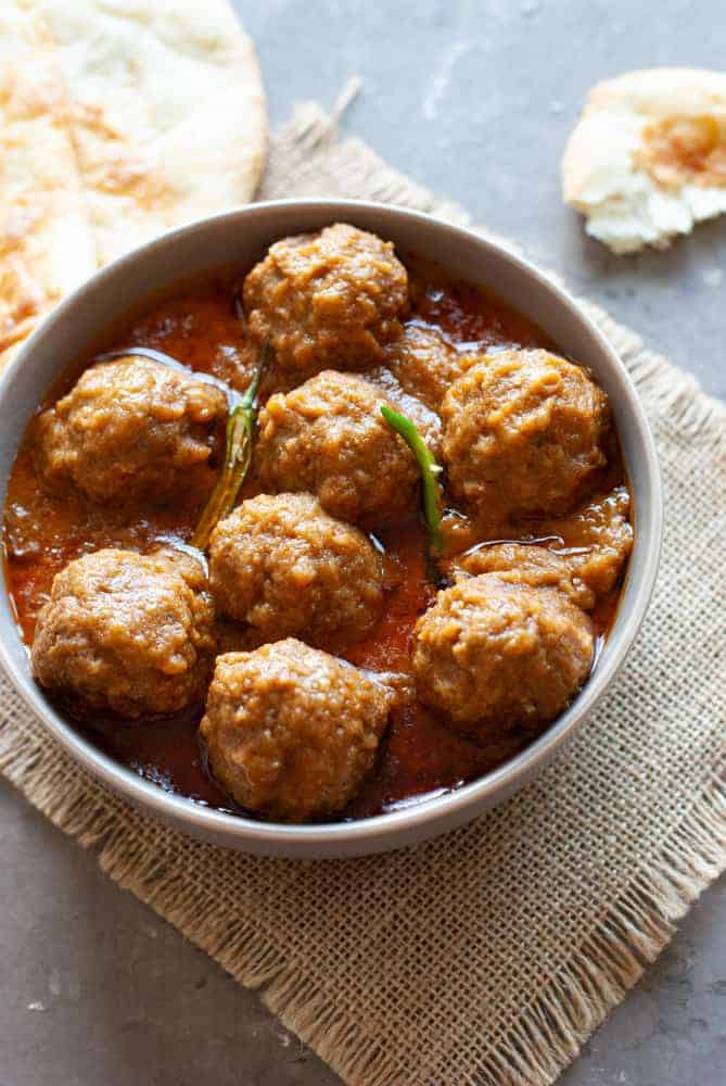 meatballs in sauce in a bowl with naan on the side