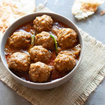 meatballs in curry in a bowl with naan on the side