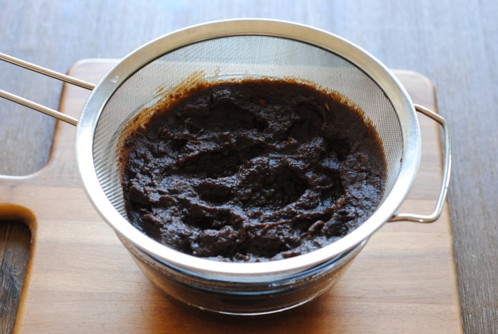 tamarind paste in a sieve over a glass bowl
