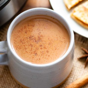 masala chai in mug with instant pot and a plate of parathas in the background