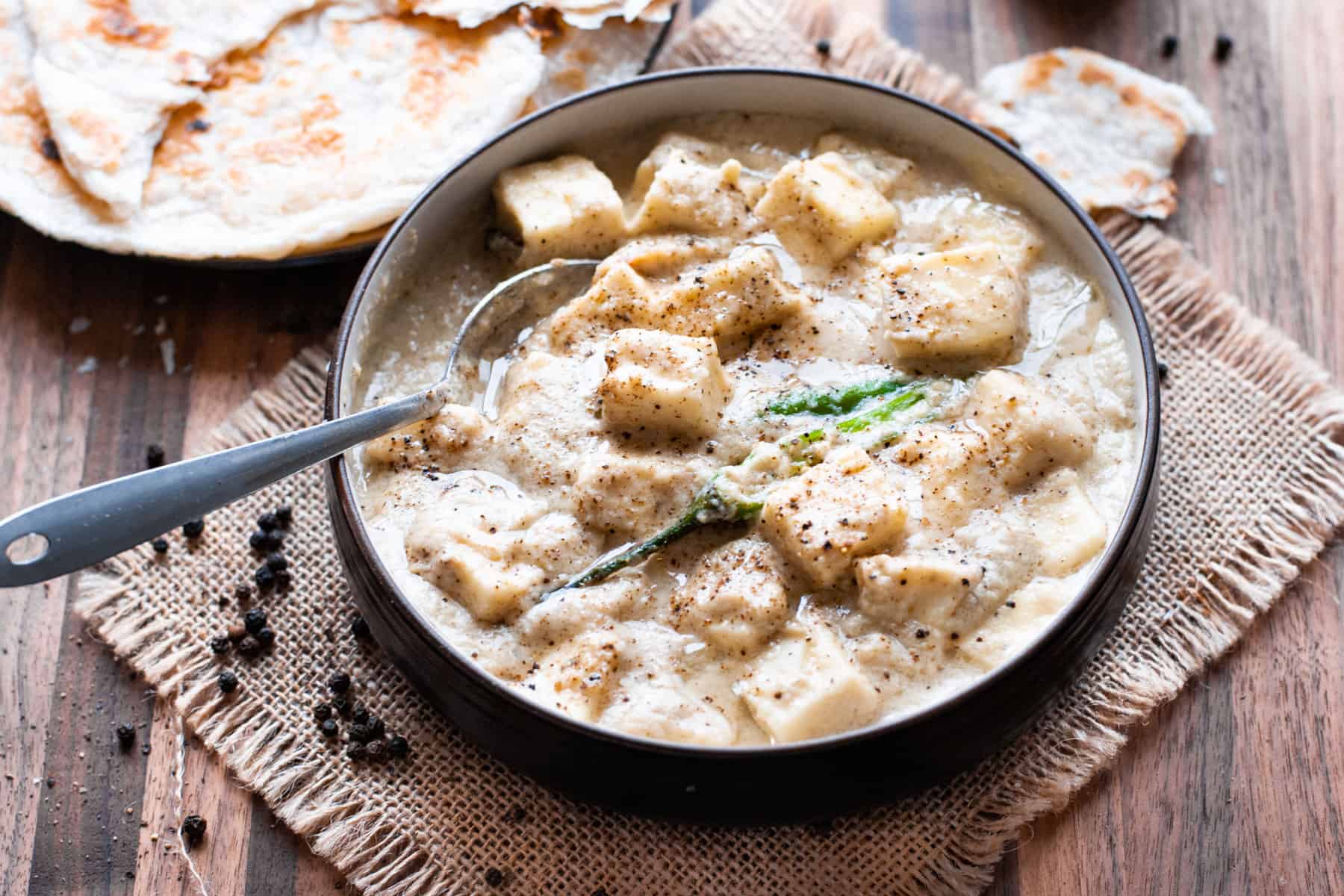 paneer in white sauce in bowl with spoon and naan on the side
