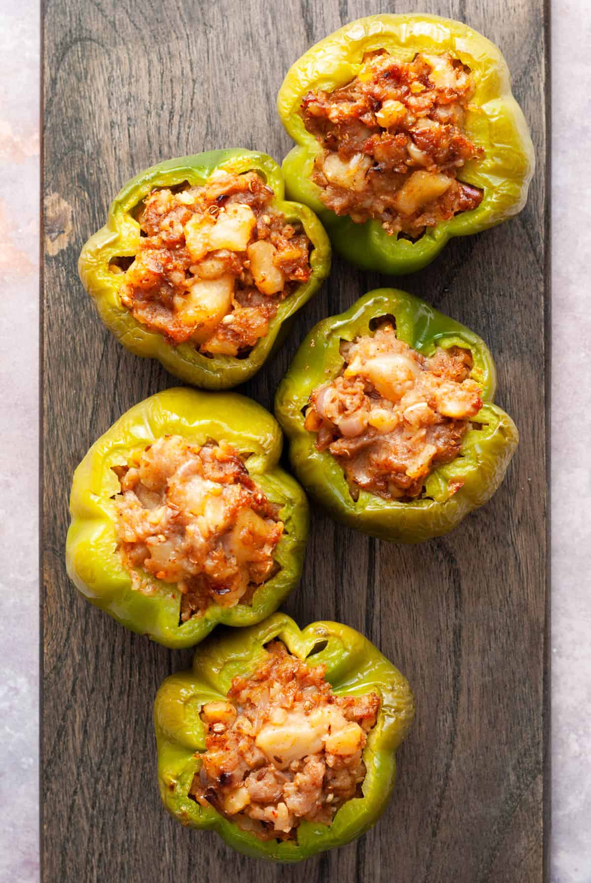 five green peppers with potato stuffing on a wooden block