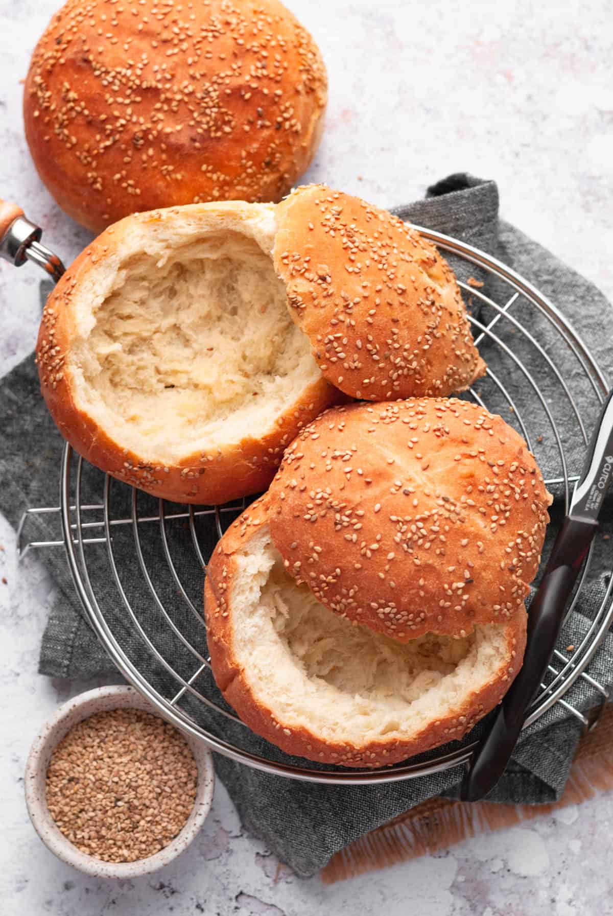 bread bowls on round wire rack and a small bowl of sesame seeds on the side