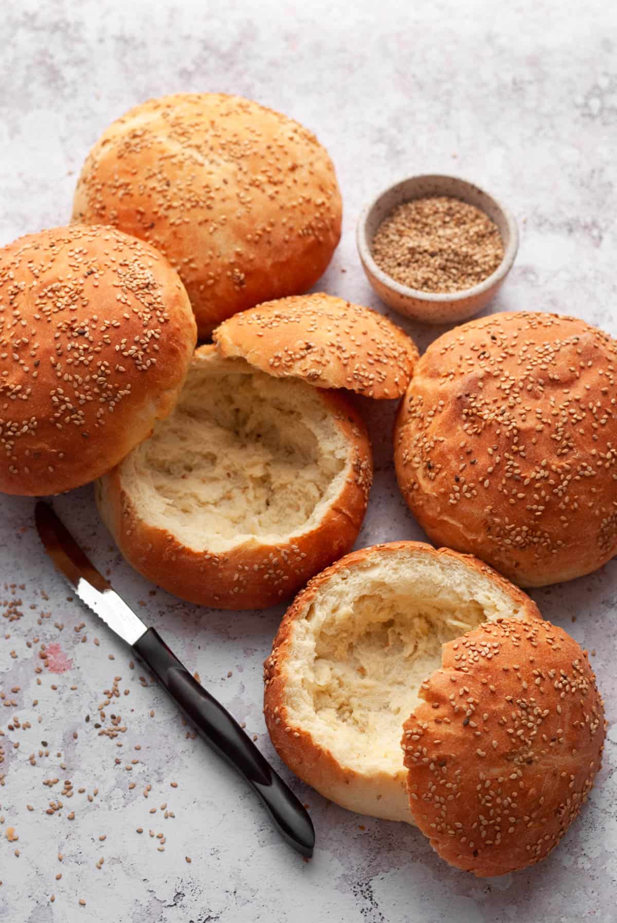 bread bowls with sesame seeds in a bowl and a knife on the side