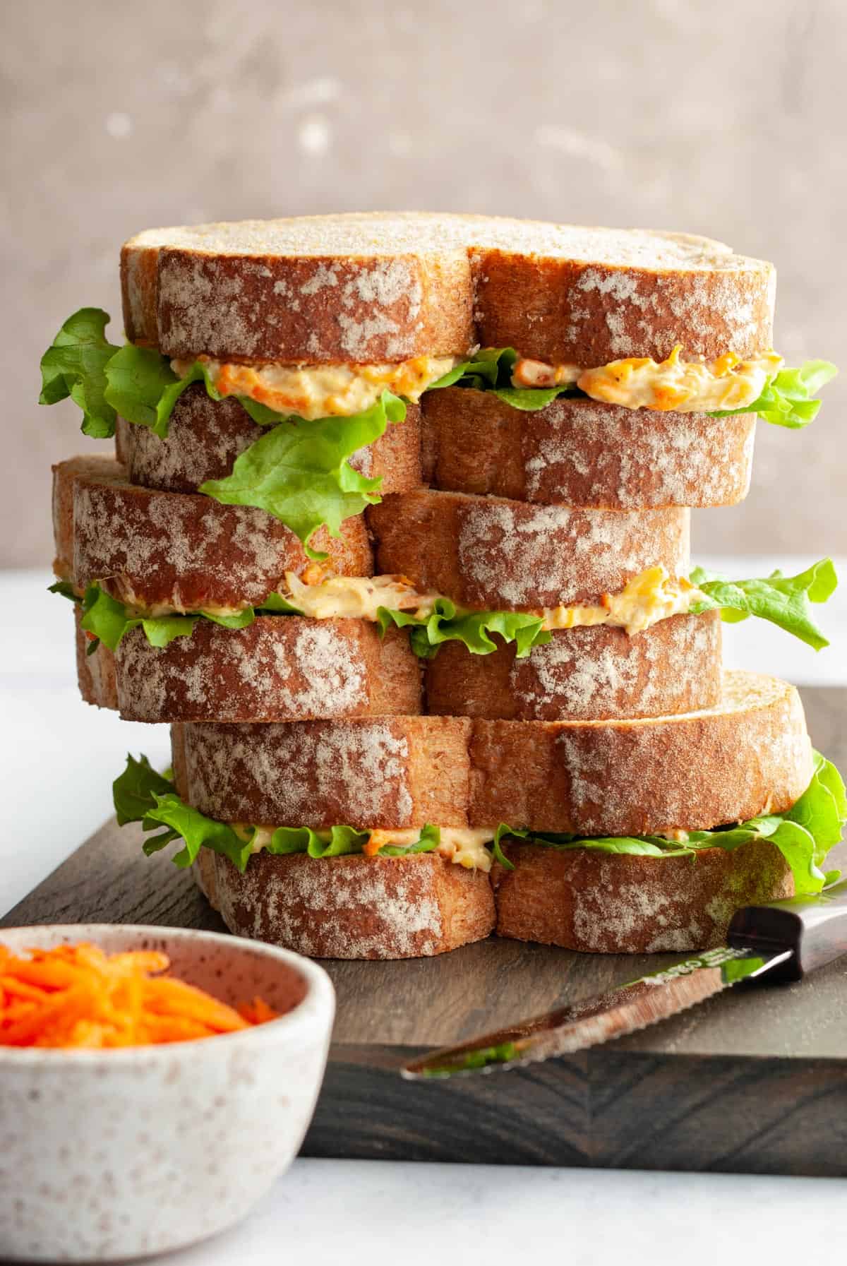 chicken mayo sandwich on a cutting board with knife and grated carrot in small bowl.