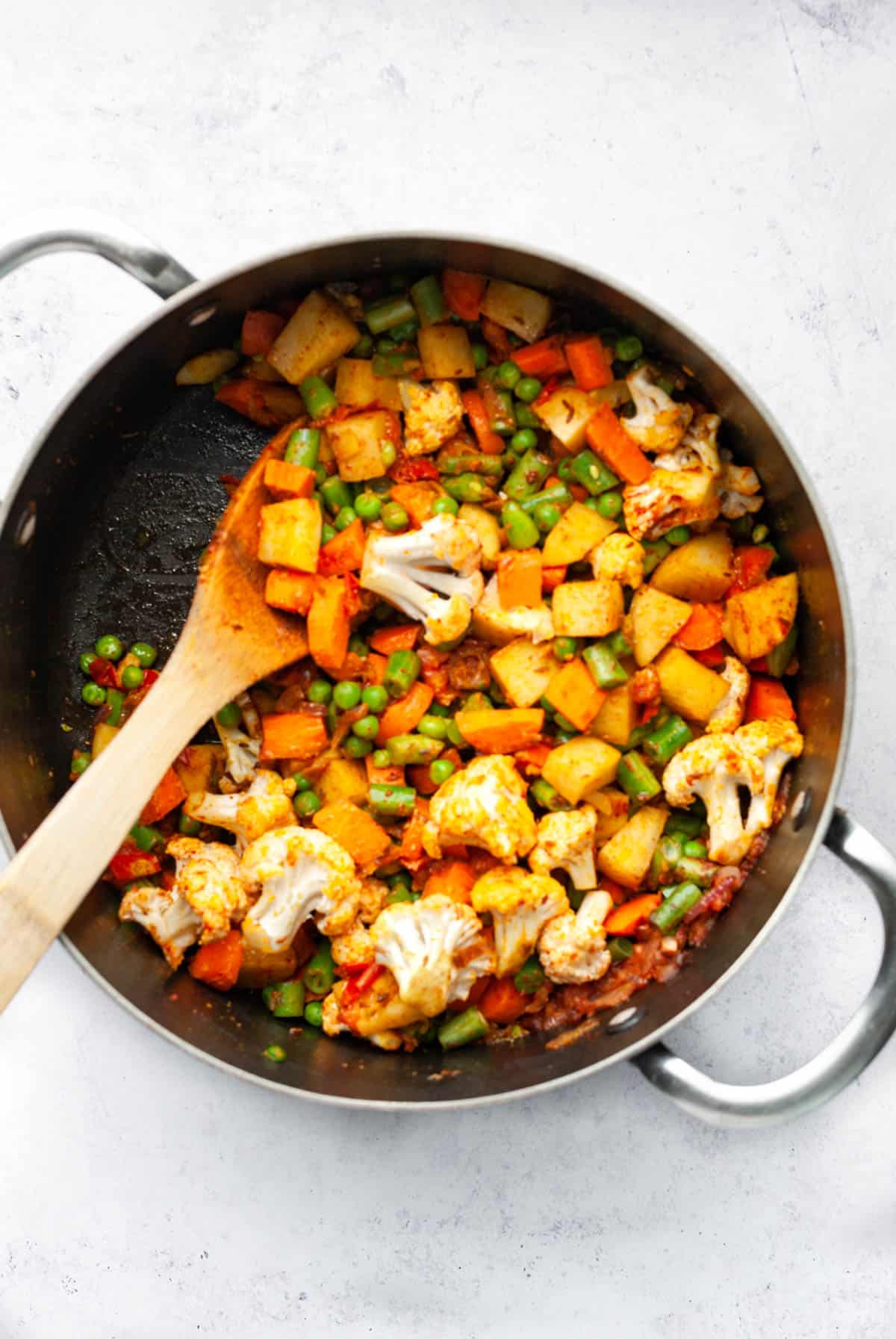 mixed vegetable sabzi in a pan with wooden spoon.