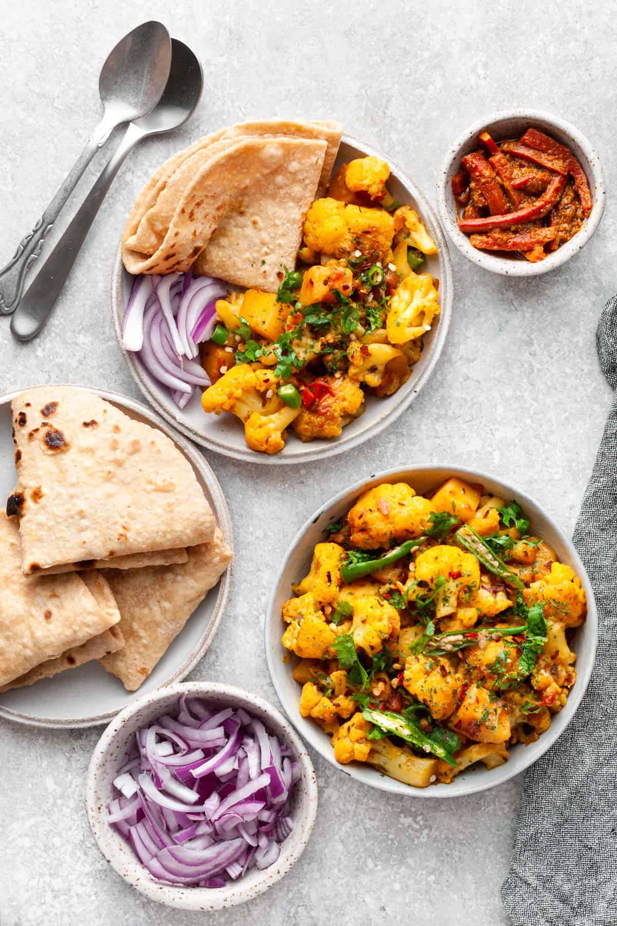 Aloo gobi in bowl with chopped onions, roti and carrot achar on the side. 