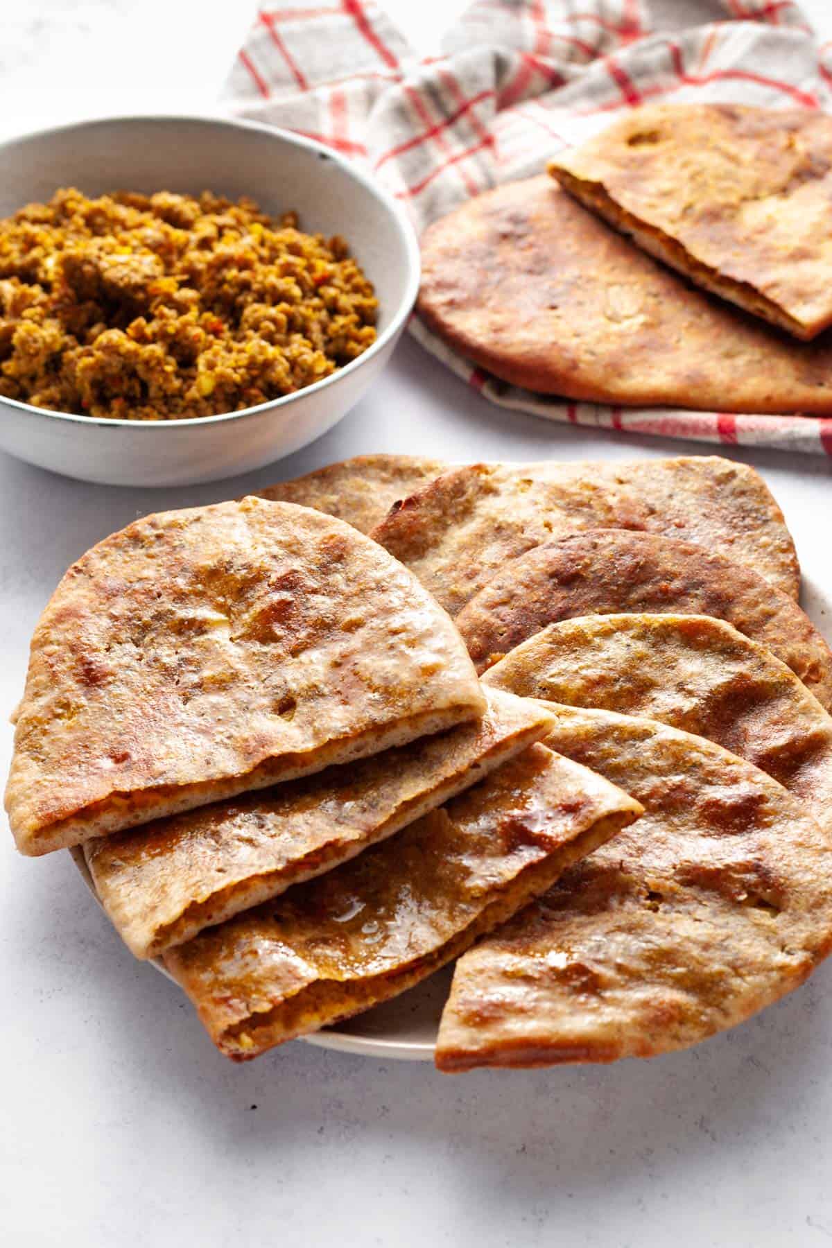 Keema naan halves in a plate with keema in bowl in background.