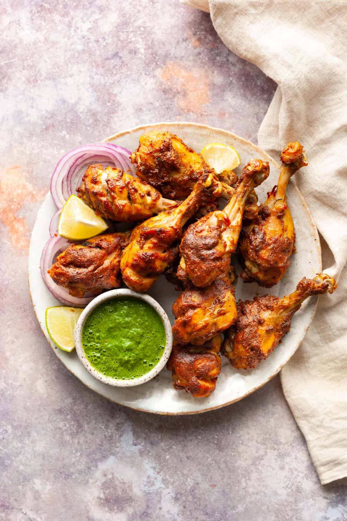 Tandoori chicken legs in a platter with cilantro chutney in a small bowl and lemon wedges.